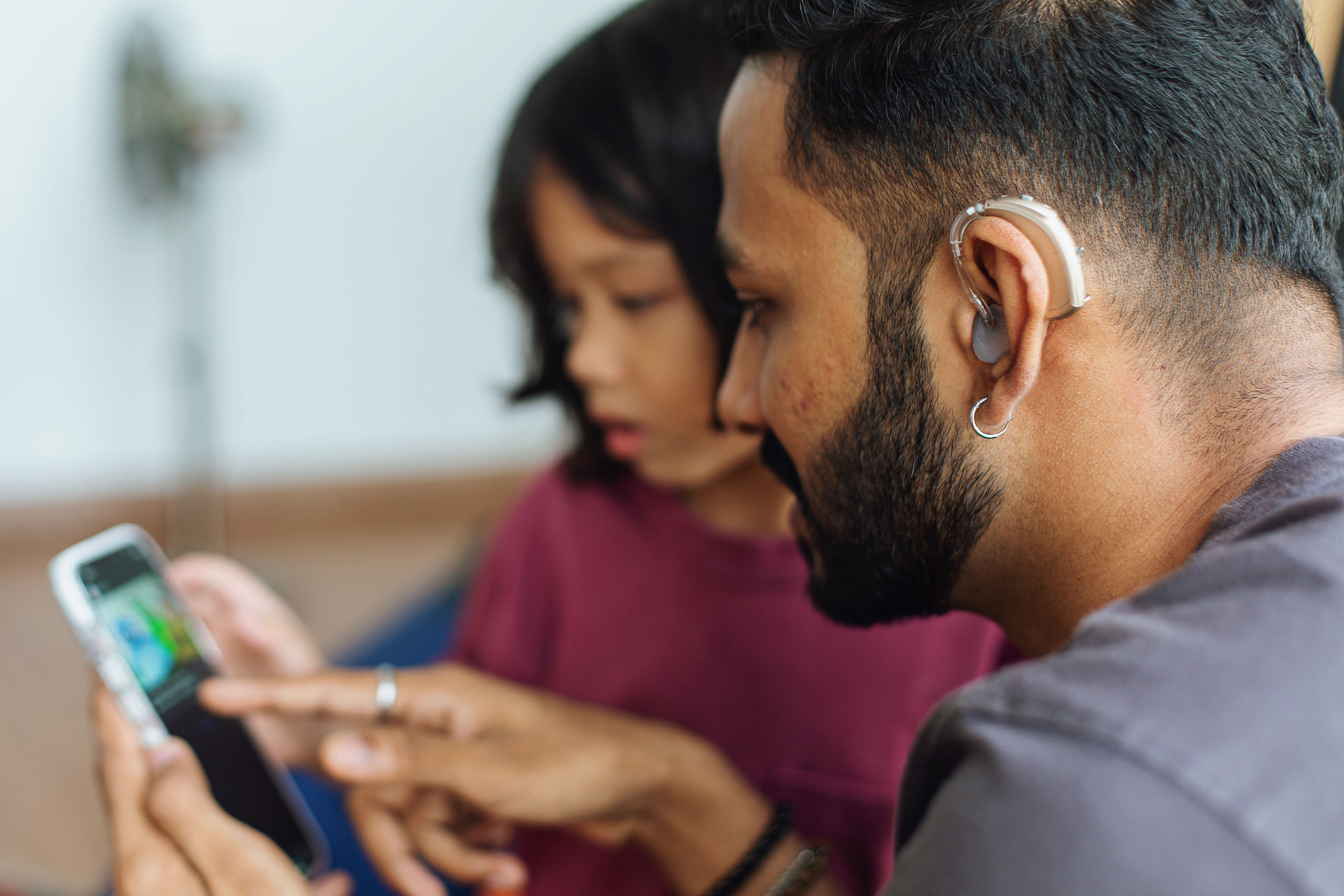 Man with Hearing Aid and Child Using Phone Closeup 